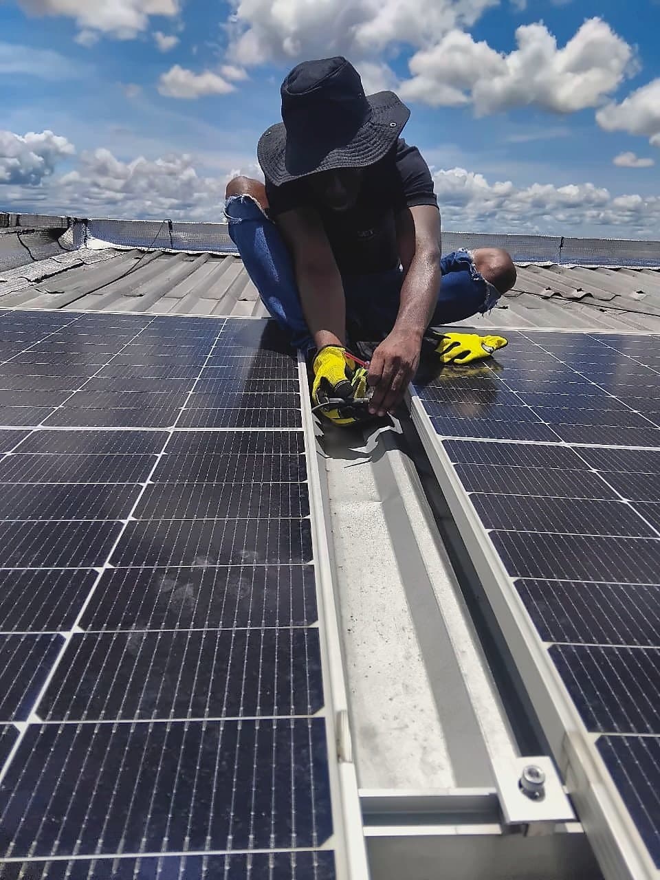 Técnico con sombrero y guantes conectando cableado entre paneles solares sobre una cubierta metálica