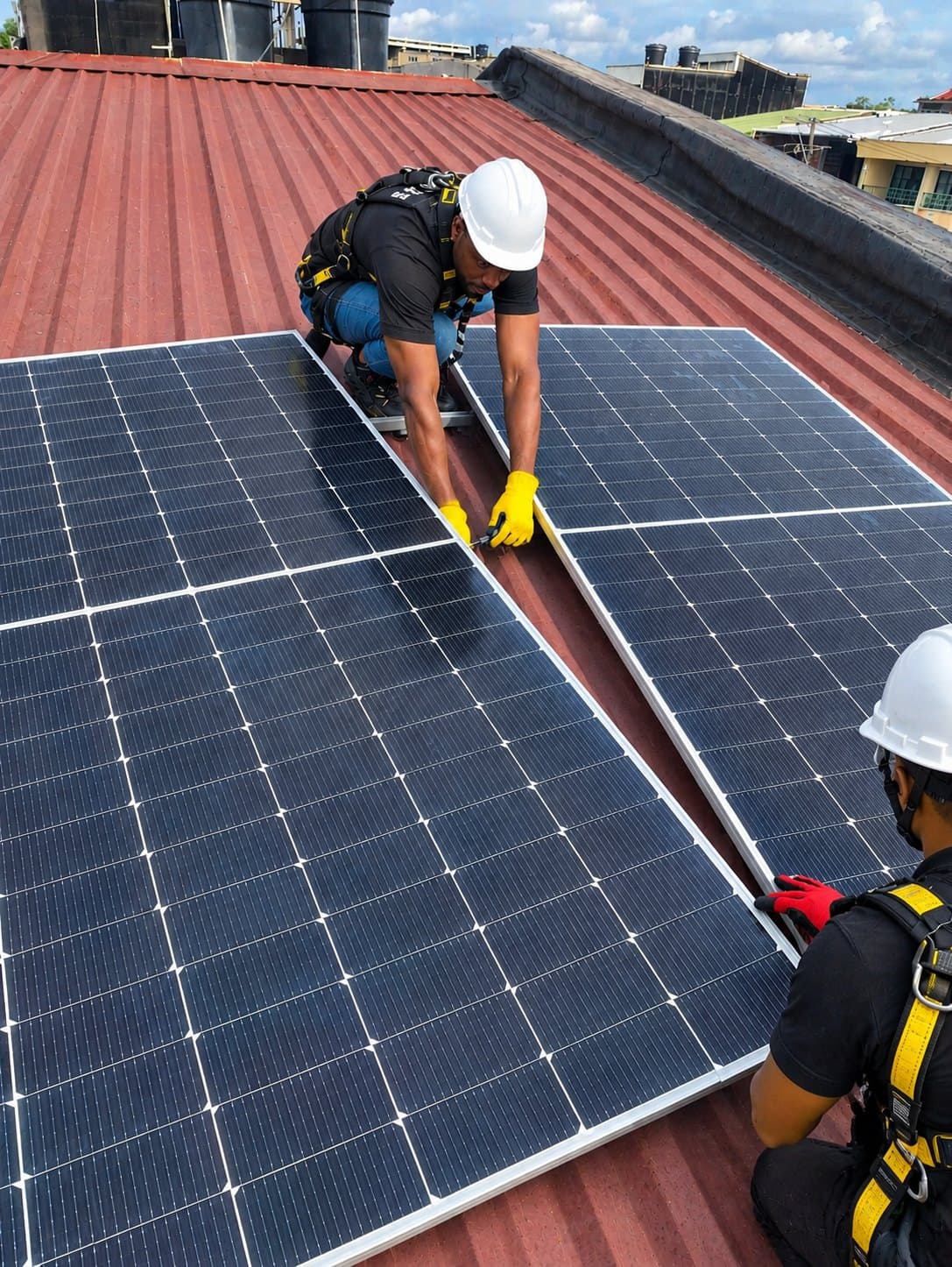 Dos técnicos con casco y arnés instalando paneles solares sobre un tejado rojo